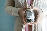 Elderly lady hands holding glass jar of coins that is labels savings.