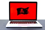 Laptop displaying a pirate flag / jolly roger on a red screen, possibly indicating malware, hackers or a different computer problem. If you like that image, consider donating at https://sharethemeal.org/donate - thanks!