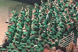 A group of graduates sitting in during commencement — all in green cap and gown.