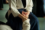 A photograph of a woman kneeling in a uniform, gripping another person’s wrist