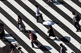 A large crossing on a road, with pedestrians walking over black and white diagonal lines