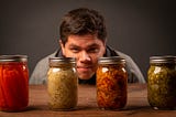 A man staring a four jars of pickles