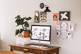 A room set up as working space with big PC and a plant beside it. On the wall there are a lamp, several wall arts, and a mirror for the decoration.