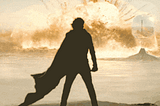 Timothee Chalamet is silhouette, robes flowing behind him, against an enormous explosion some distance away across a desert plain
