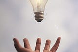Hand reaching out to catch a lit lightbulb