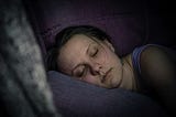 The photo shows a woman sleeping on her right side, her head on a pillow. The room is dark, indicating she is sleeping at night.
