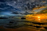 Cloudy sunrise on the horizon as waves break in the foreground