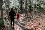 A father walking behind his daughter along a path in the woods