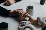 two people holding hands with two coffee cups on the table next to them