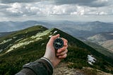 A man holding a compass in the middle of mountains
