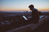 A man works at a laptop while sitting on a rooftop