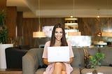 woman sitting on a couch, smiling, laptop on her lap