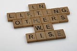 scrabble cubes spelling out “In lifting others we rise.”