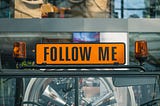 A sign between two unactivated flashing orange lights that says “Follow Me”