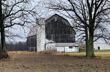 An old barn backed by trees in winter