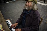 Elderly man playing an upright piano on a street