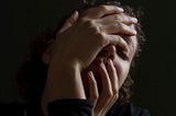 woman’s face mostly covered by her hands, looking stressed
