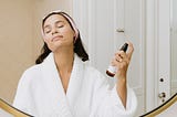 A woman in a bathrobe using a natural skincare product.