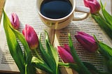 a white cup of black coffee surrounded by beautiful lillat flowers on an open book