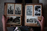 An old photo album opened on black and white pictures. On the right page, two vertical pictures of people on horses and a horizontal picture of a cabin. On the left page, two vertical pictures of people and a horizontal picture of two kids in front of an old car.