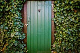 An image of a green door, surrounded in foilage