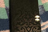 Black velvet patterned notebook on a turquoise and blue afgan.