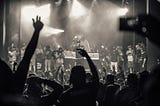 Black and white image of a crowd with hands in the air at a hip hop concert