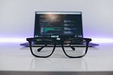 A pair of glasses in front of an open laptop