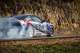 A white Holden (GM) race car emblazoned with blue and red on a race track burning out its rear tires, smoke billowing from the rear tires