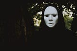 A cloaked figure in a plain white mask covering the face, intended to be symbolic of an unknown threat