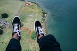 Photo by Colton Jones on Unsplash — an aerial view of a shoreline but with two legs dangling in the scene as if the person were floating above the world.