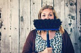 A comical picture of a woman holding a broom upside-down in front of her face so you can only see her eyes.