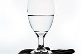 A dark hand open palm up while holding a wine glass. The Glass is half filled with water.