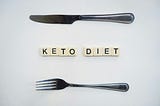 Tiles spell out KETO DIET. There is a knife  above the tiles and a fork below it.