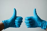 Two thumbs up while wearing medical examination gloves.