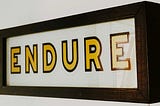 Wall sign that say “Endure” in gold coloured letters