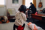 A child in the foreground, with parent working on laptop in background