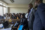Kenyan lawyers stand around a computer for a virtual meeting.