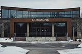 A community college building with the word “COMMONS” above the front door in a snowy landscape.