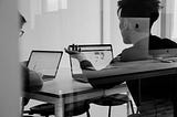 Black & white photo of 2 people meeting at their laptops.