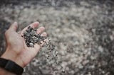 An extended hand dropping gravel on the ground (the ground is blurry).