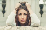 A woman bunching up her hair on her head with her hands as she looks nervously into the camera.