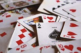 A deck of cards is spread across a table. On top, an ace of spades is visible.