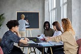 Anonymous man writing on chalkboard near group of diverse students at table