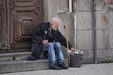Old man resting on the steps of a church with his cane and bag of belongings