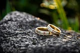 Two gold wedding rings, embedded with diamonds, on what appears to be a gray rock.