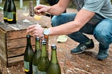 Person opening wine bottles with a hammer and nails