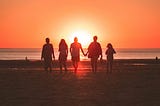 a group of people walk towards a sunset on a beach
