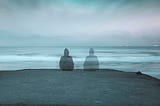 A bluish-grey picture, one person sitting on the left with a mirror shadow on the right, facing the ocean.