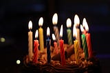 Photo of birthday cake and lit candles on black background.